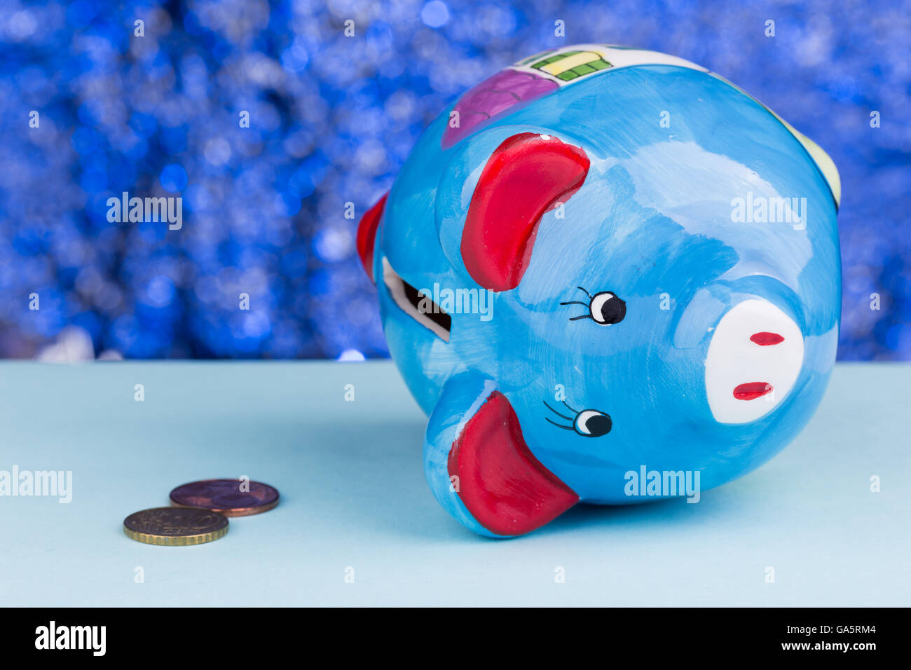 Blue piggy bank on a blue background: it's on its side with a few penny ...