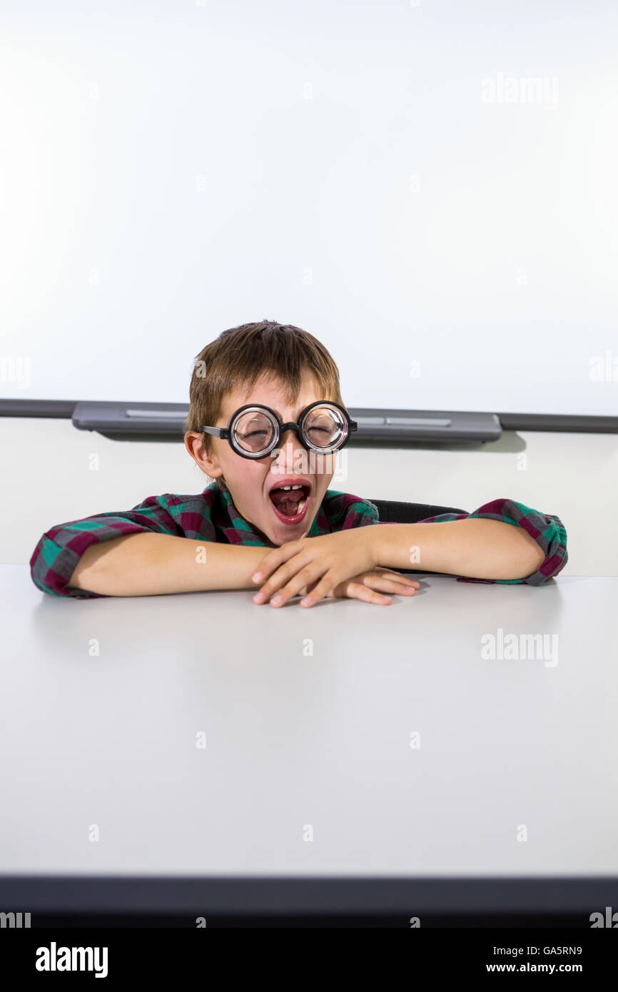 Boy yawning while sitting at table in classroom Stock Photo