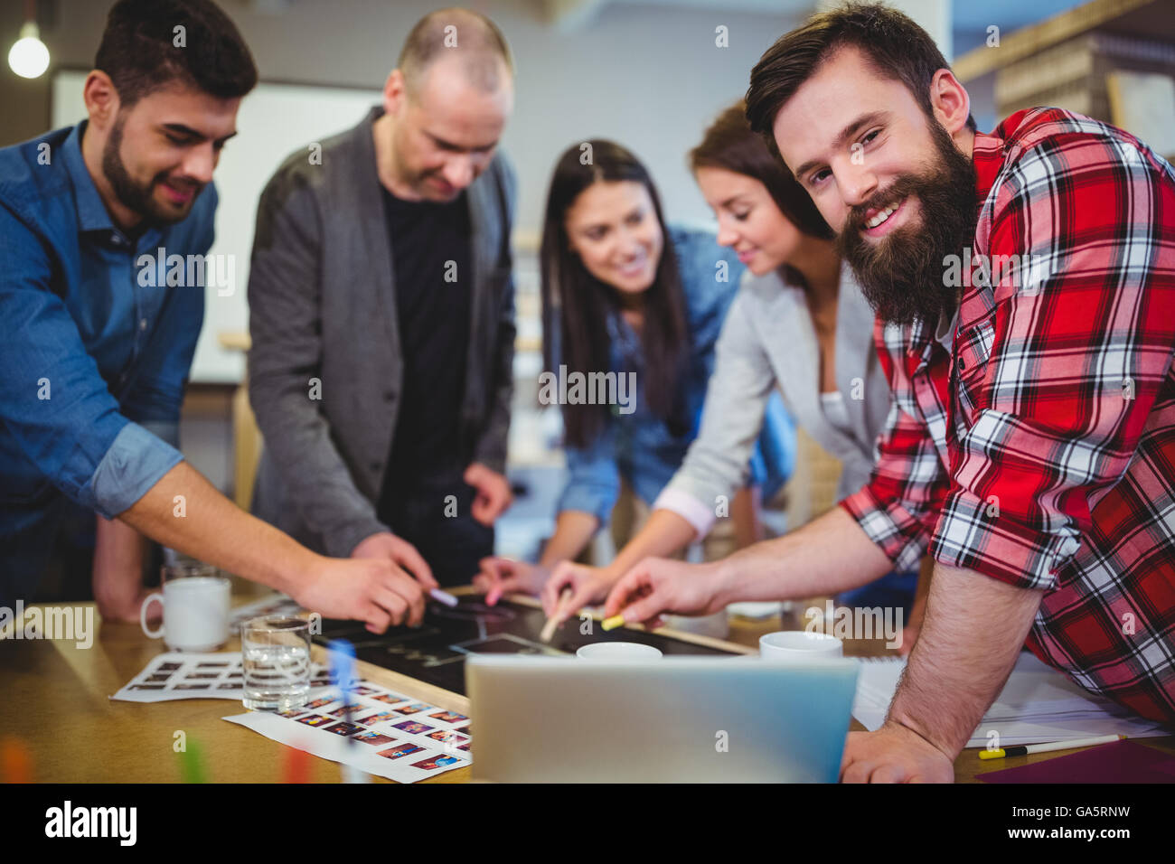 Hipster smiling while colleagues drawing on blackboard Stock Photo