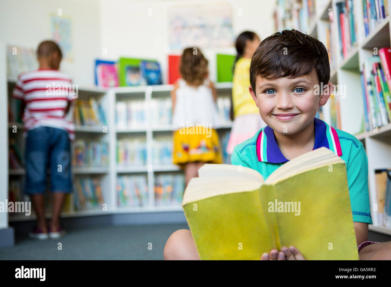 Portrait of boy holding book at school library Stock Photo - Alamy