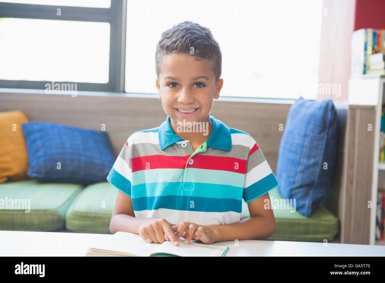 Schoolboy sitting on table and reading book in library Stock Photo