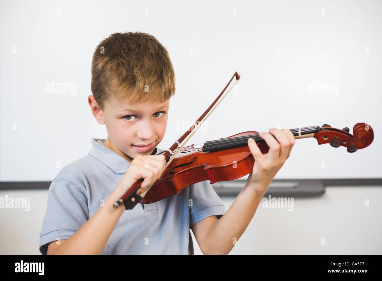 Portrait of smiling schoolboy playing violin in classroom Stock Photo