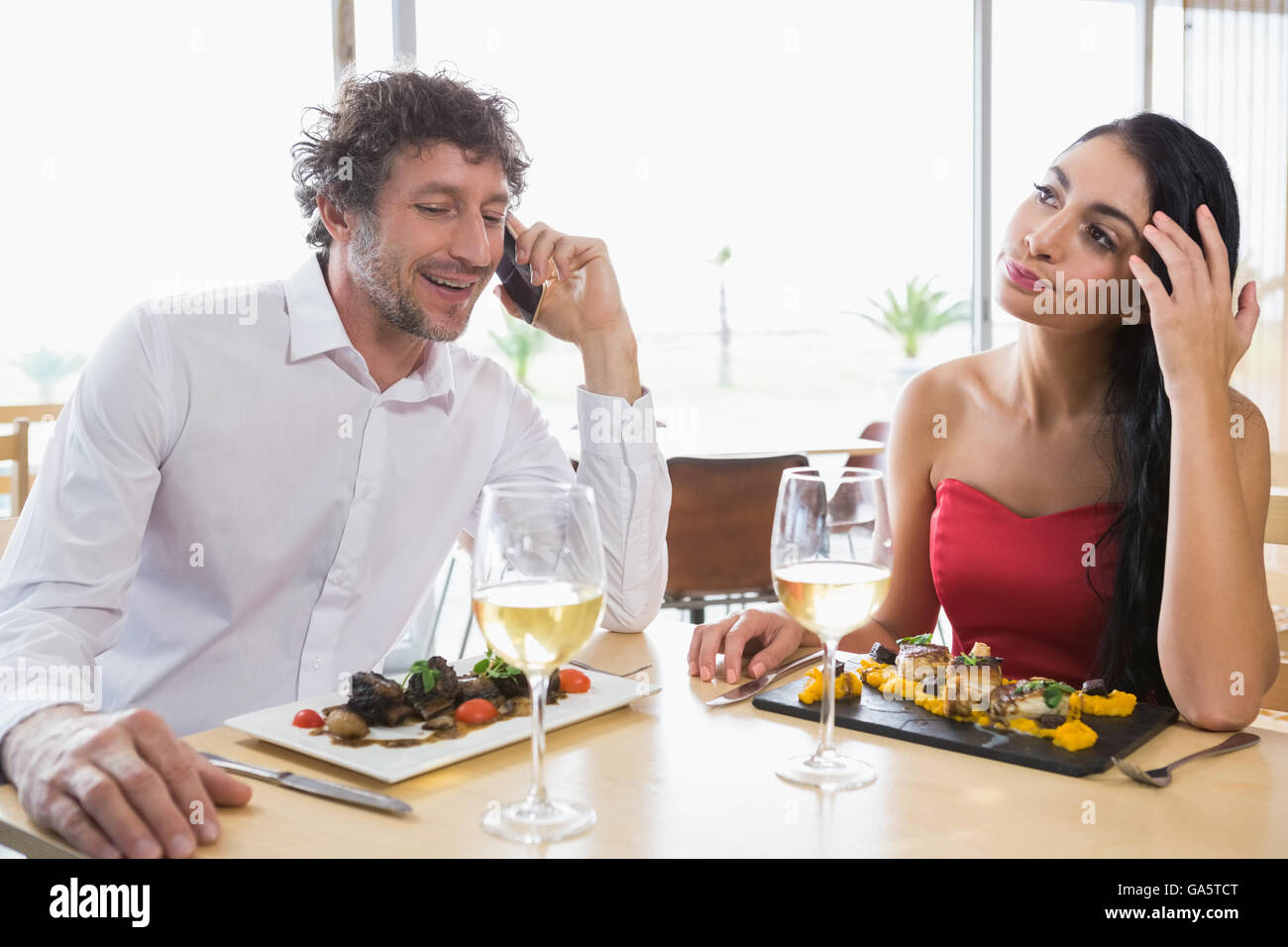 Woman sitting while man talking mobile phone Stock Photo