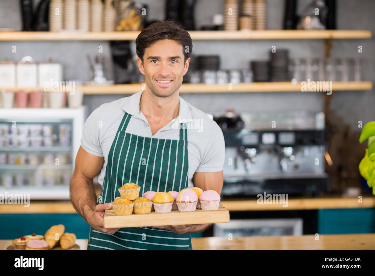Portrait of smiling waiter holding a tray of cupcakes Stock Photo