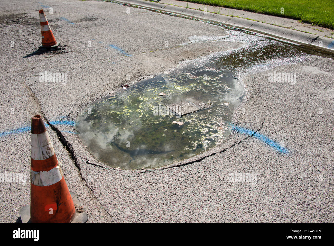 Water leak in the street causes the pavement to sink along with the loss of water. Stock Photo