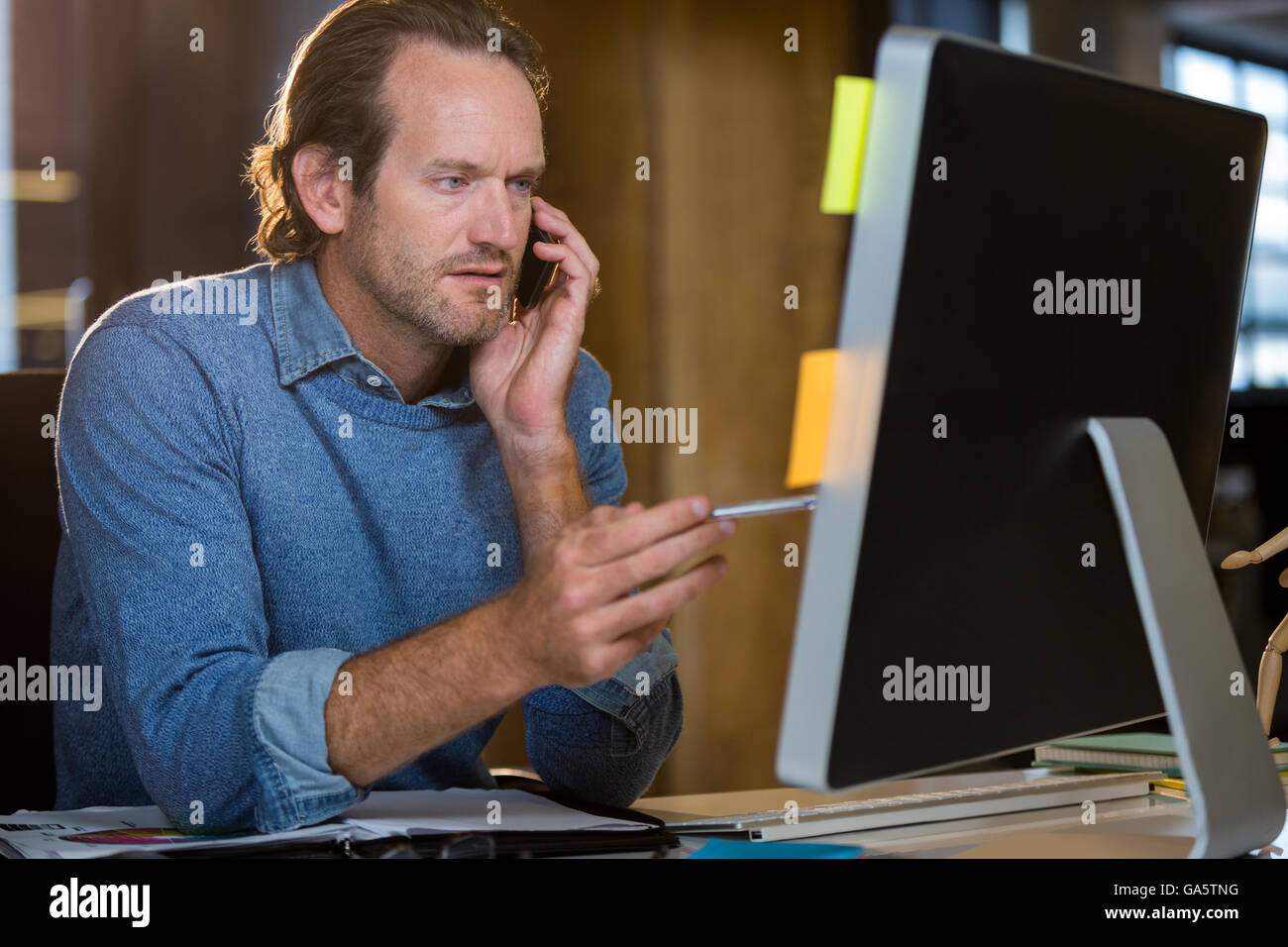 Businessman looking at monitor while talking on cellphone Stock Photo