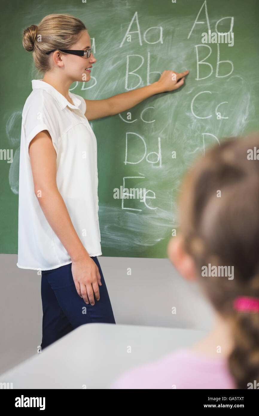 Smiling teacher teaching kids on chalkboard in classroom Stock Photo