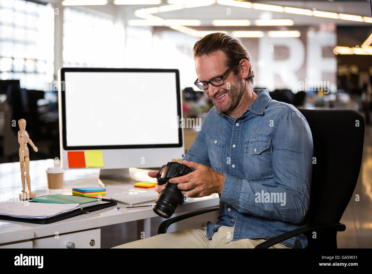 Businessman holding camera while sitting by desk Stock Photo