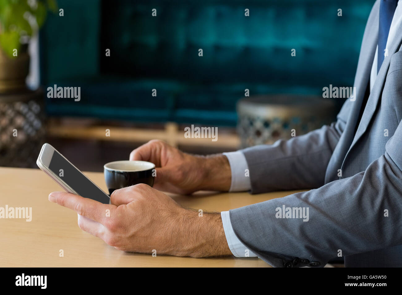 Mid-section of businessman using mobile phone while having a cup of tea ...