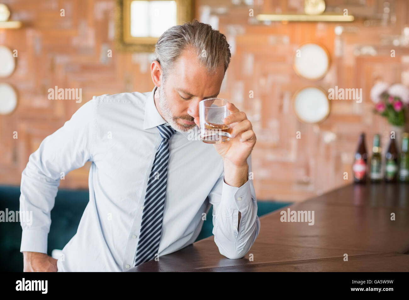 Businessman clutching whiskey glass to forehead Stock Photo