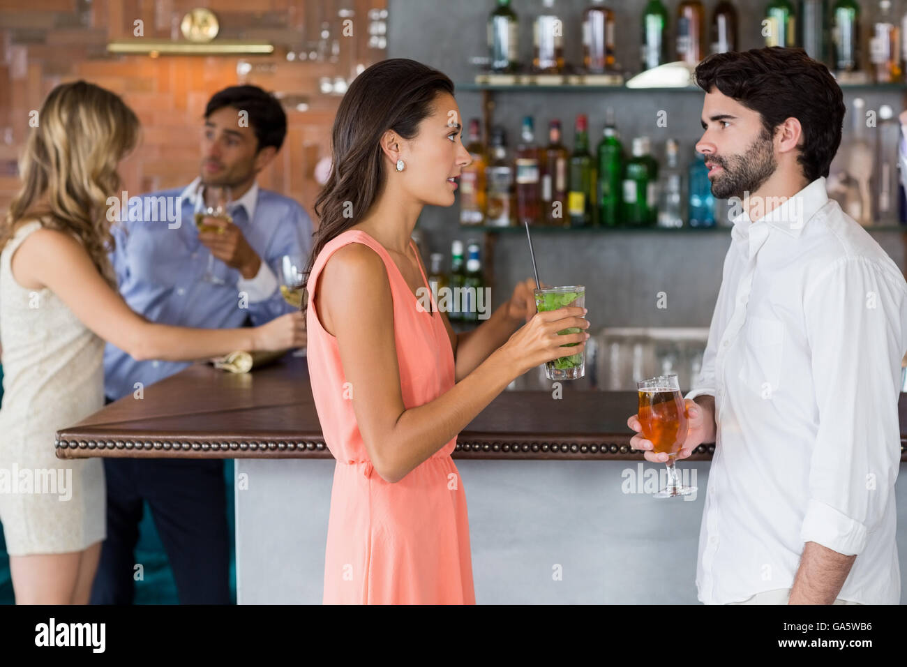 Couple holding a glass of cocktail in front of bar counter Stock Photo