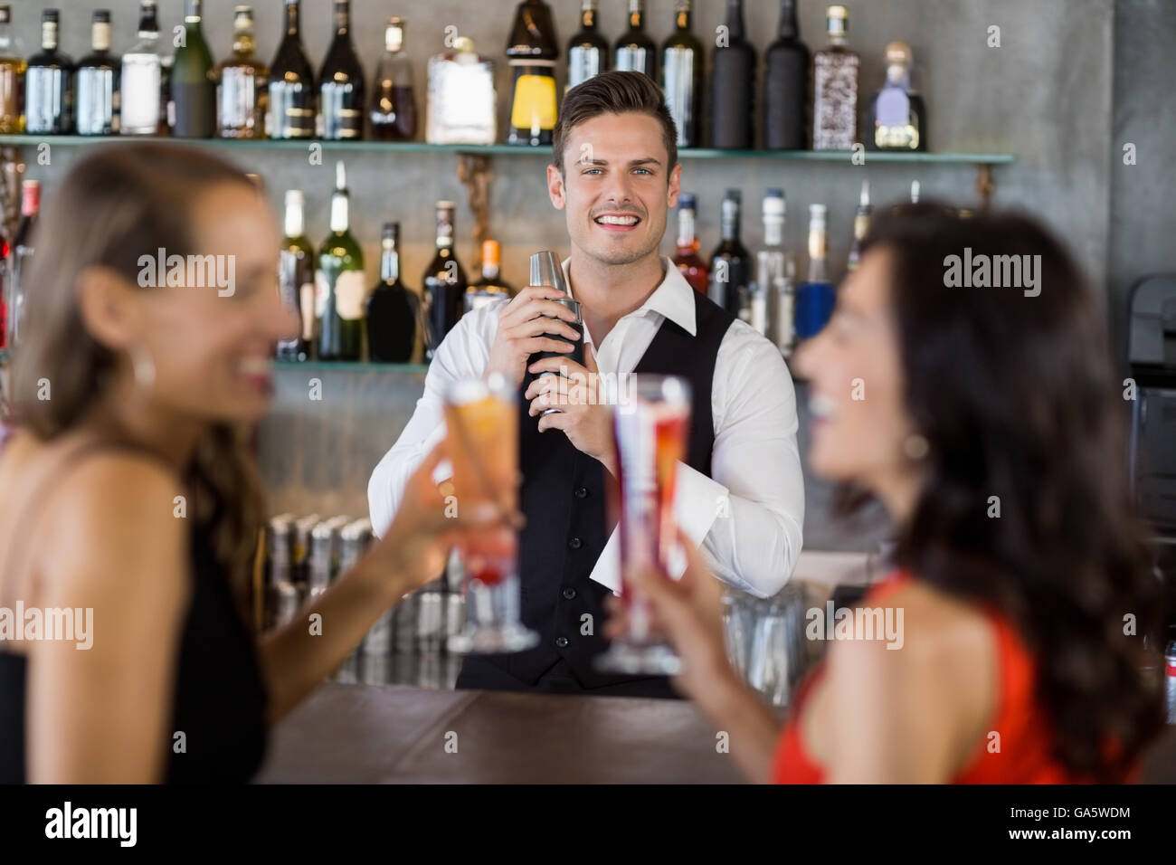 Two women having cocktail while a waiter preparing cocktail with cocktail shaker Stock Photo