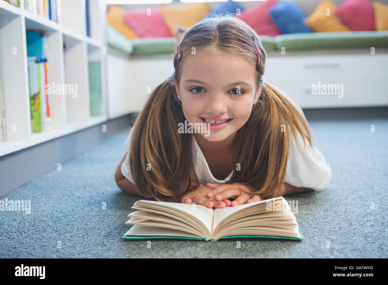 Schoolgirl lying on floor and reading a book in library Stock Photo - Alamy