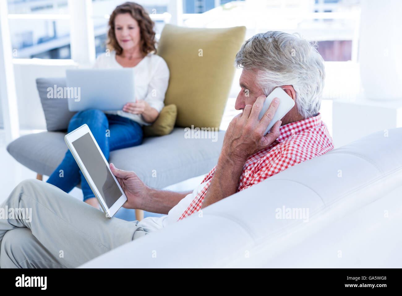 Mature man talking on phone while holding tablet at home Stock Photo