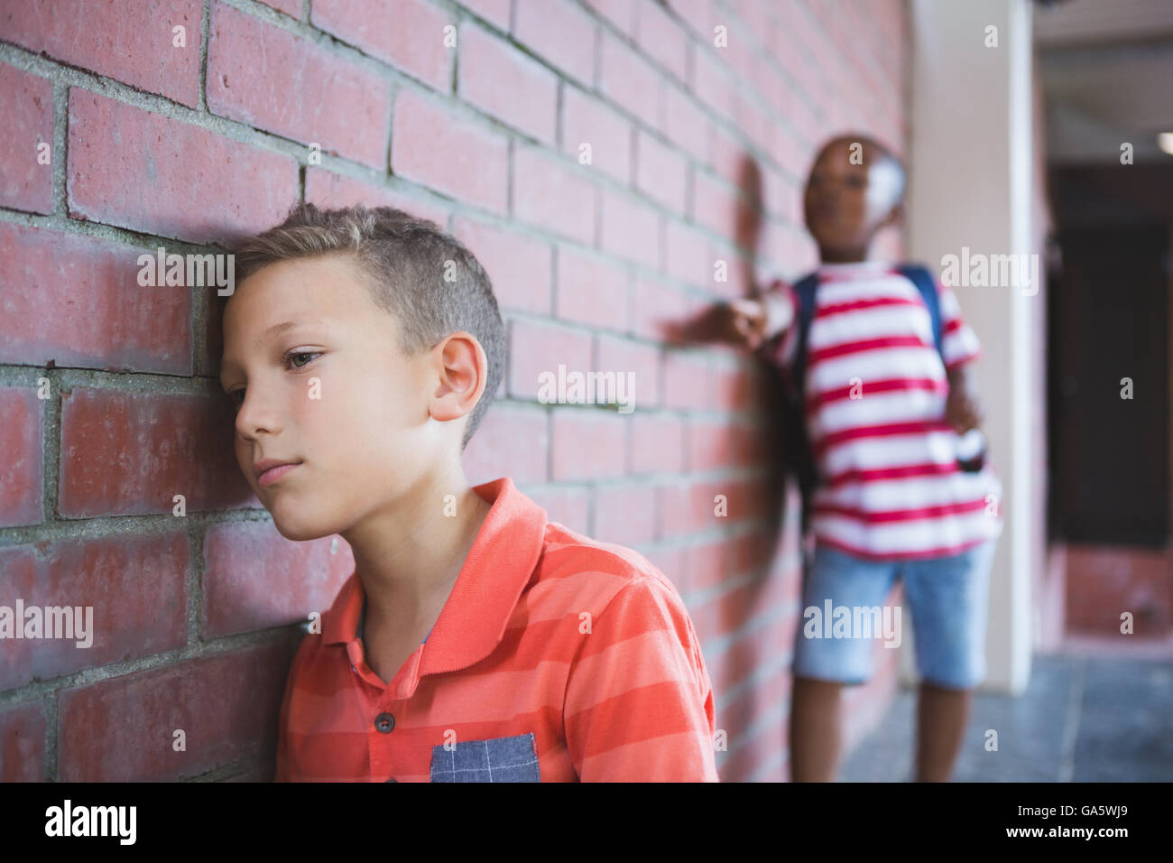 Schoolkid bullying a sad boy in corridor Stock Photo