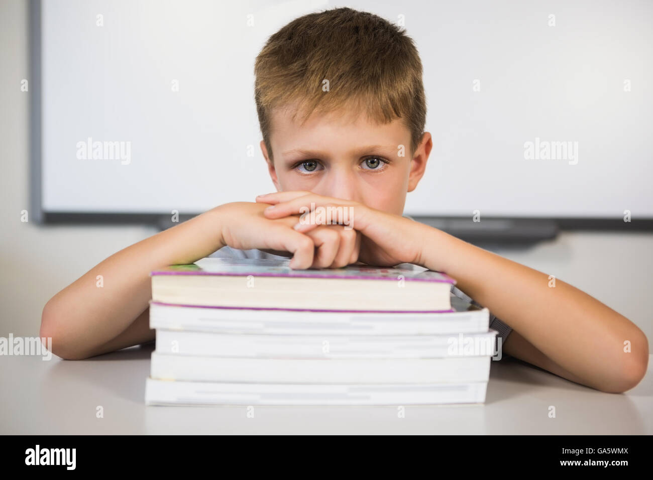 Portrait of sad schoolboy leaning on stack of books in class room Stock ...