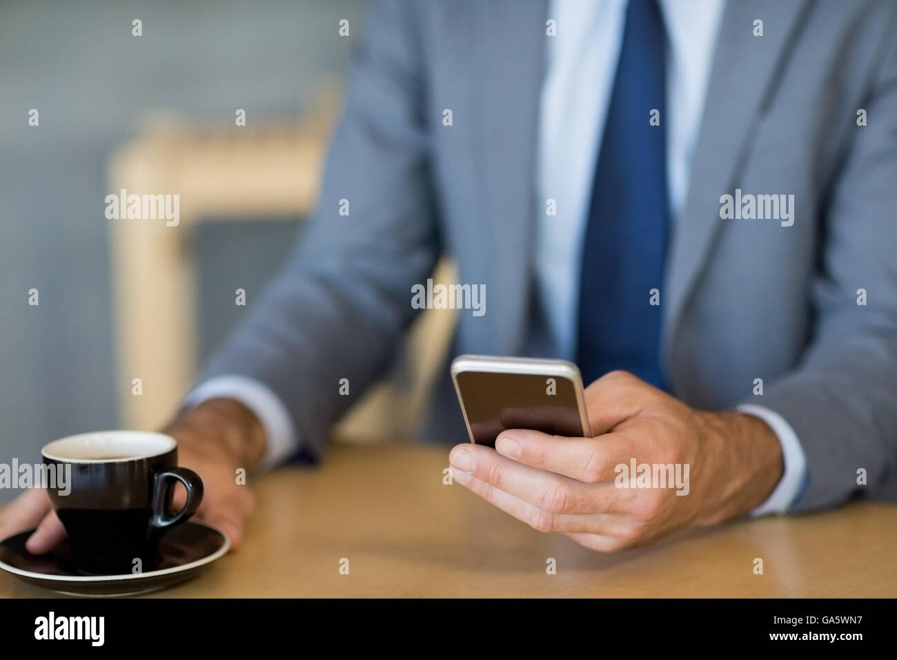 Mid-section of businessman using mobile phone while having a cup of tea ...
