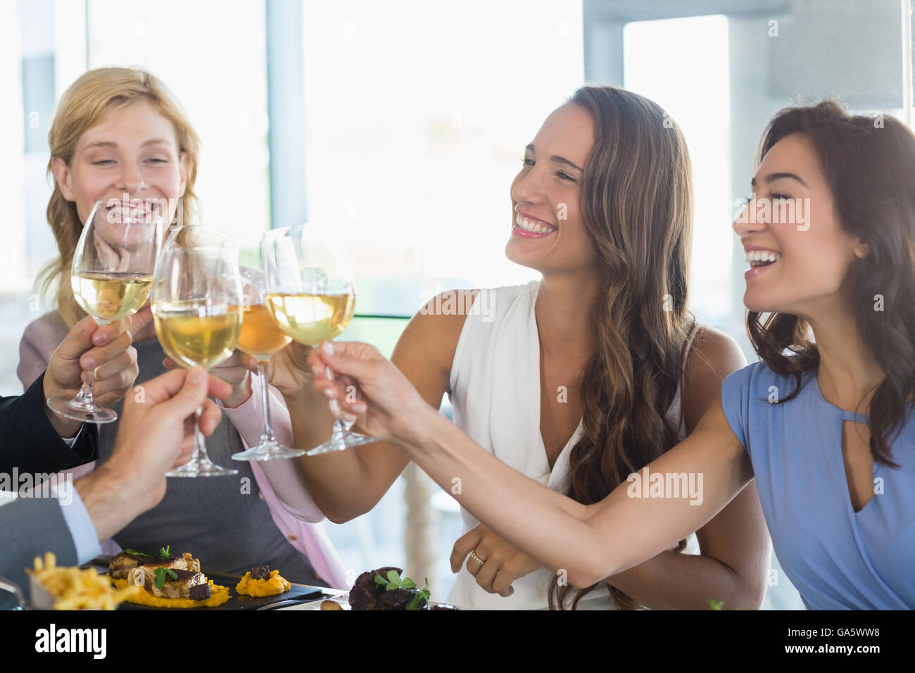 Happy female colleagues toasting beer glasses while having lunch Stock Photo