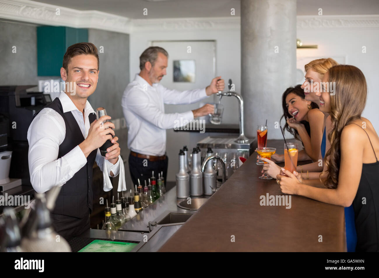 Beautiful women having cocktail while waiter preparing cocktail with cocktail shaker Stock Photo