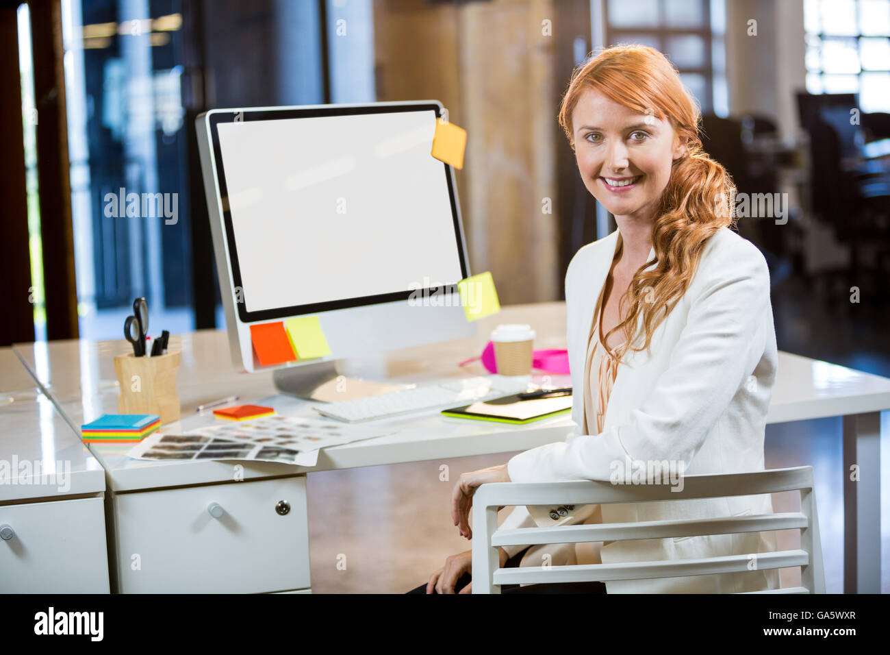 Businesswoman smiling while sitting by computer desk Stock Photo