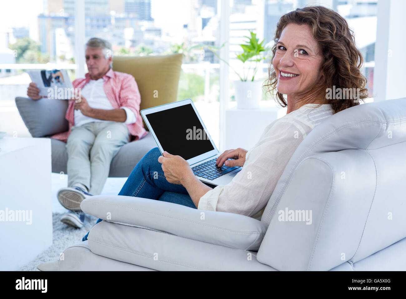 Smiling woman with laptop while mature man reading newspaper Stock Photo