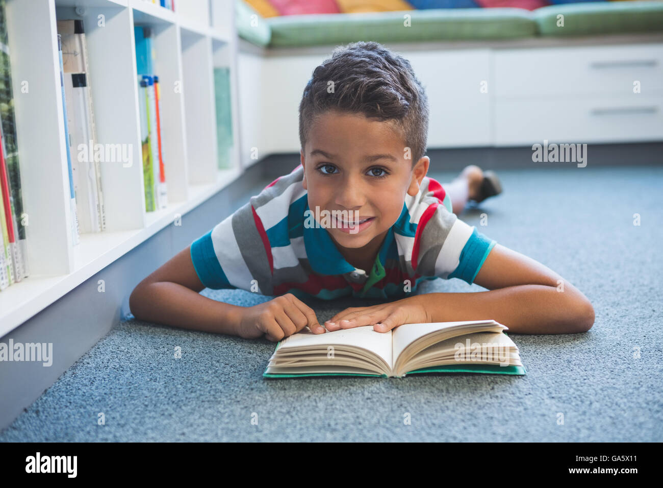 Schoolboy lying on floor and reading a book in library Stock Photo - Alamy