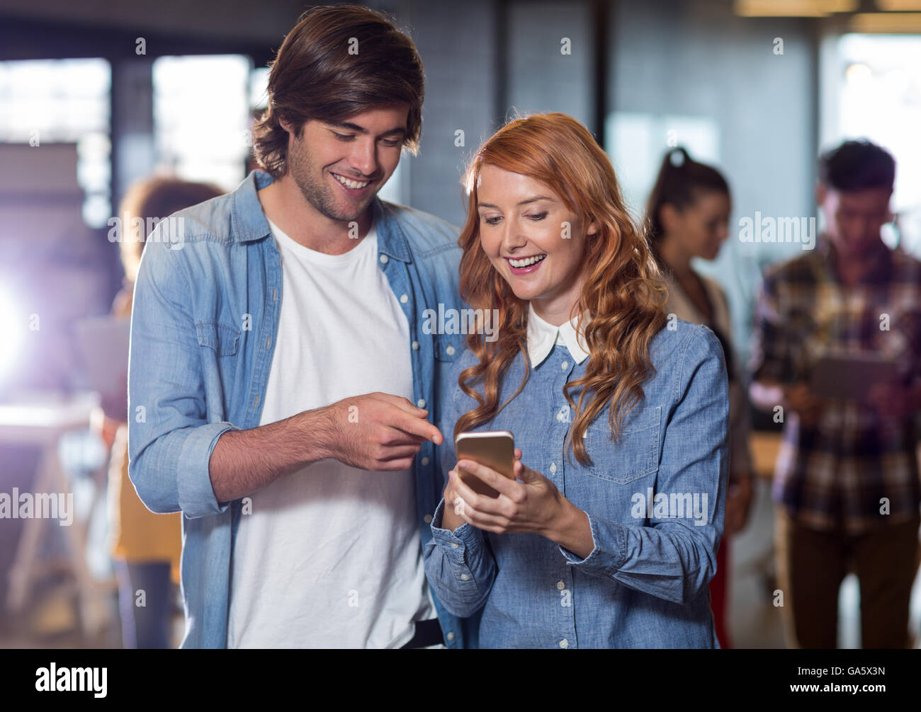 Smiling colleagues discussing while using mobile phone in office Stock Photo
