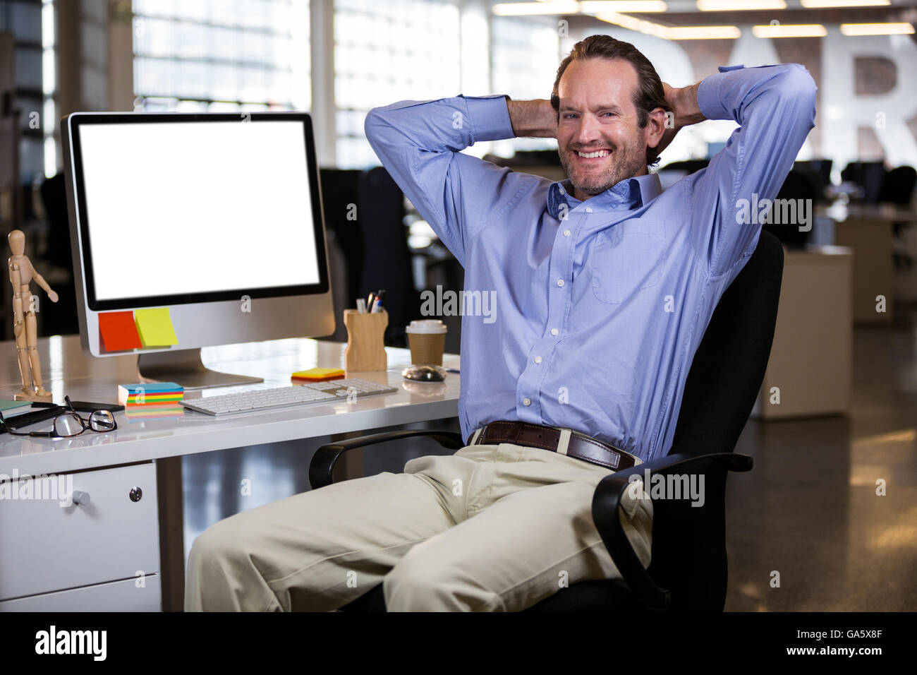 Businessman sitting with hands behind head by desk Stock Photo