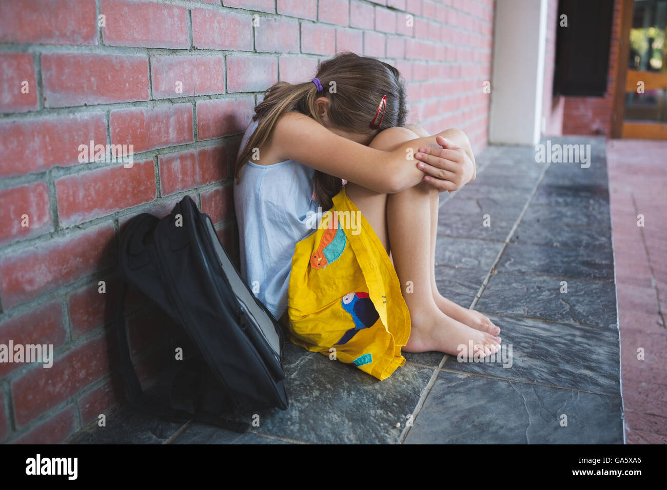 Sad schoolkid sitting alone in corridor Stock Photo