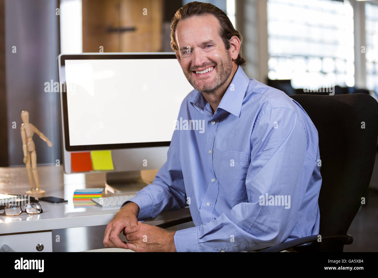 Smiling businessman sitting by computer desk Stock Photo