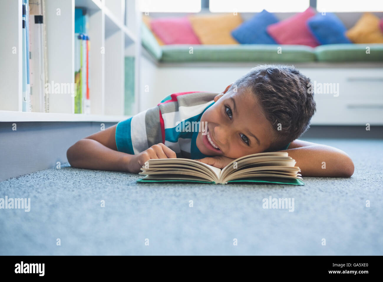 Schoolboy lying on floor and reading a book in library Stock Photo - Alamy