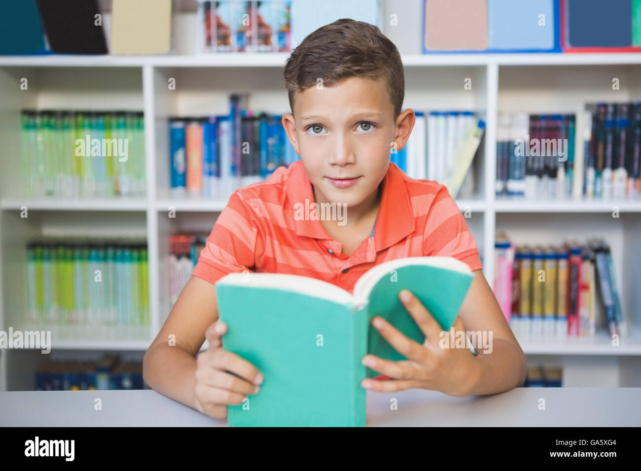 Schoolboy sitting on table and reading book in library Stock Photo