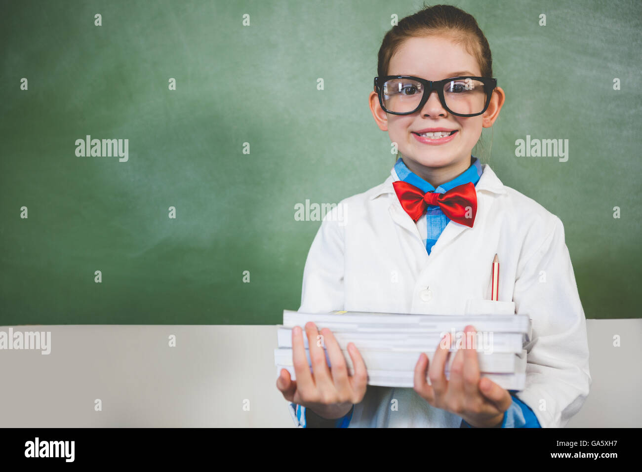 Portrait of smiling girl standing with a stack of books in classroom Stock Photo