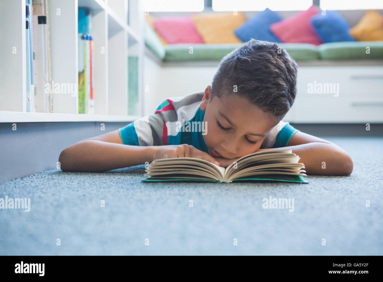 Schoolboy lying on floor and reading a book in library Stock Photo - Alamy