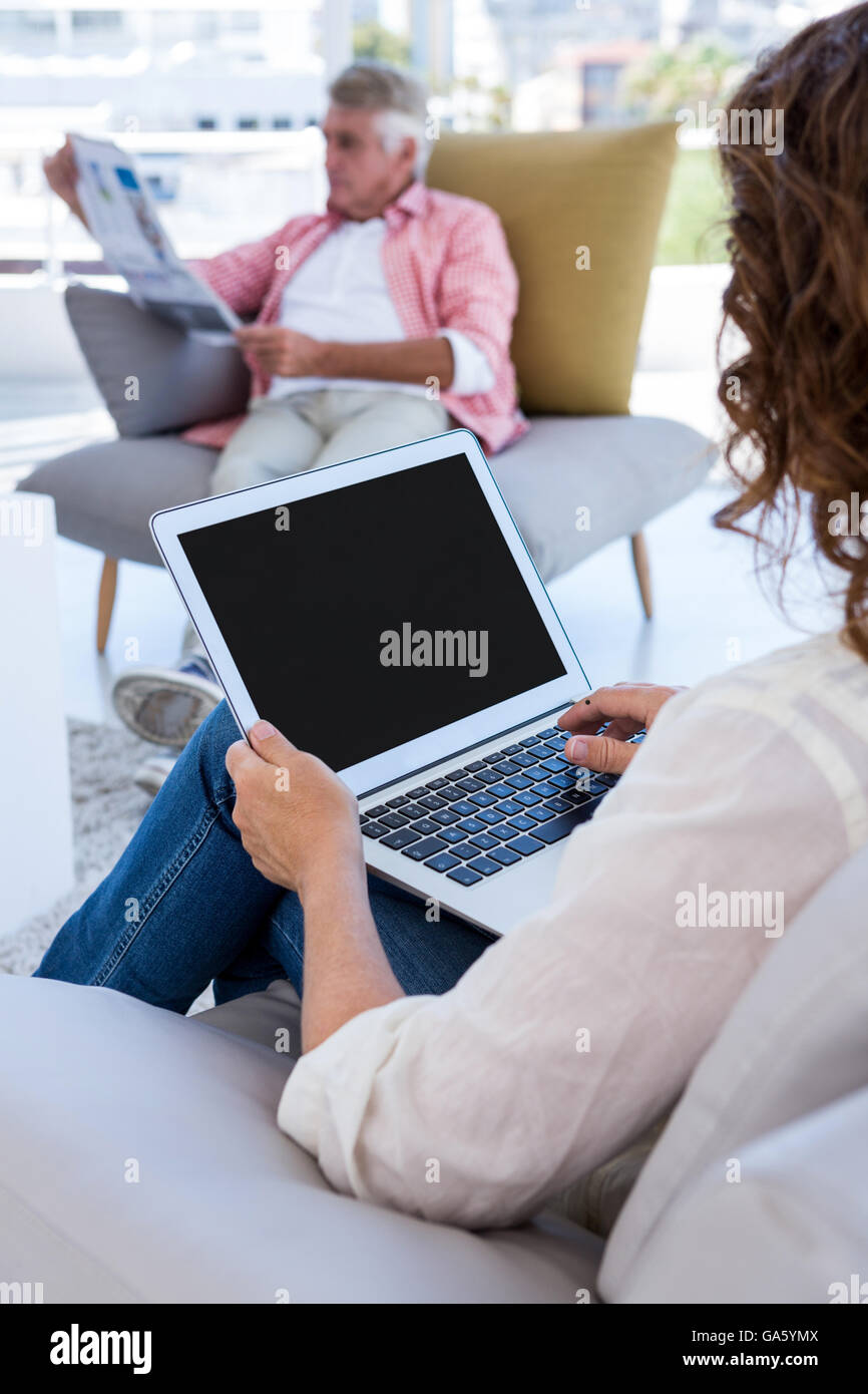 Woman using laptop while mature man reading newspaper Stock Photo