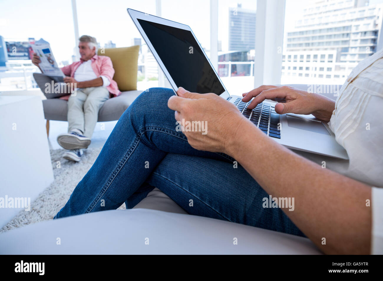 Midsection of Woman using laptop while man reading newspaper Stock Photo