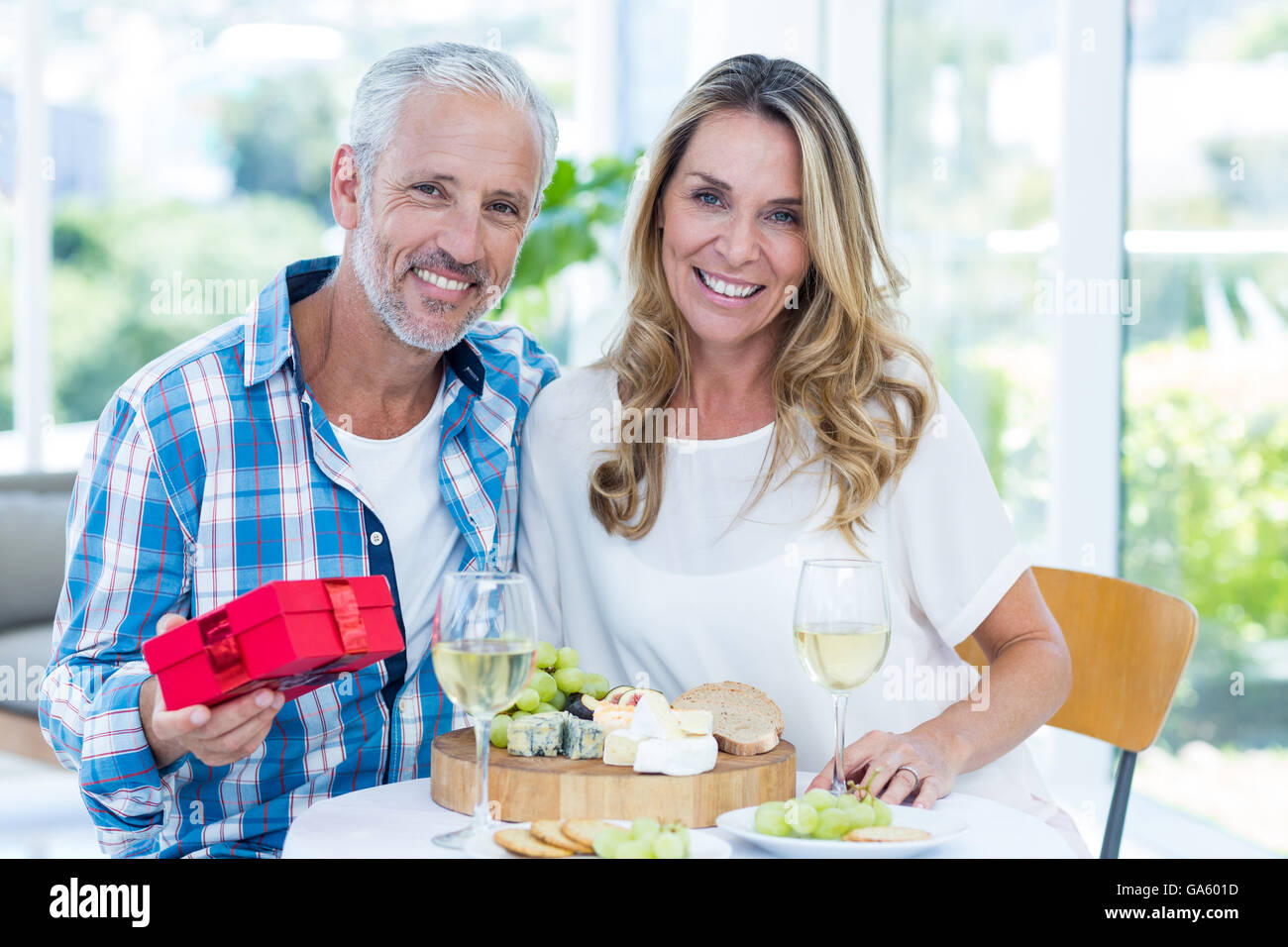 Mature man holding gift while sitting beside wife Stock Photo