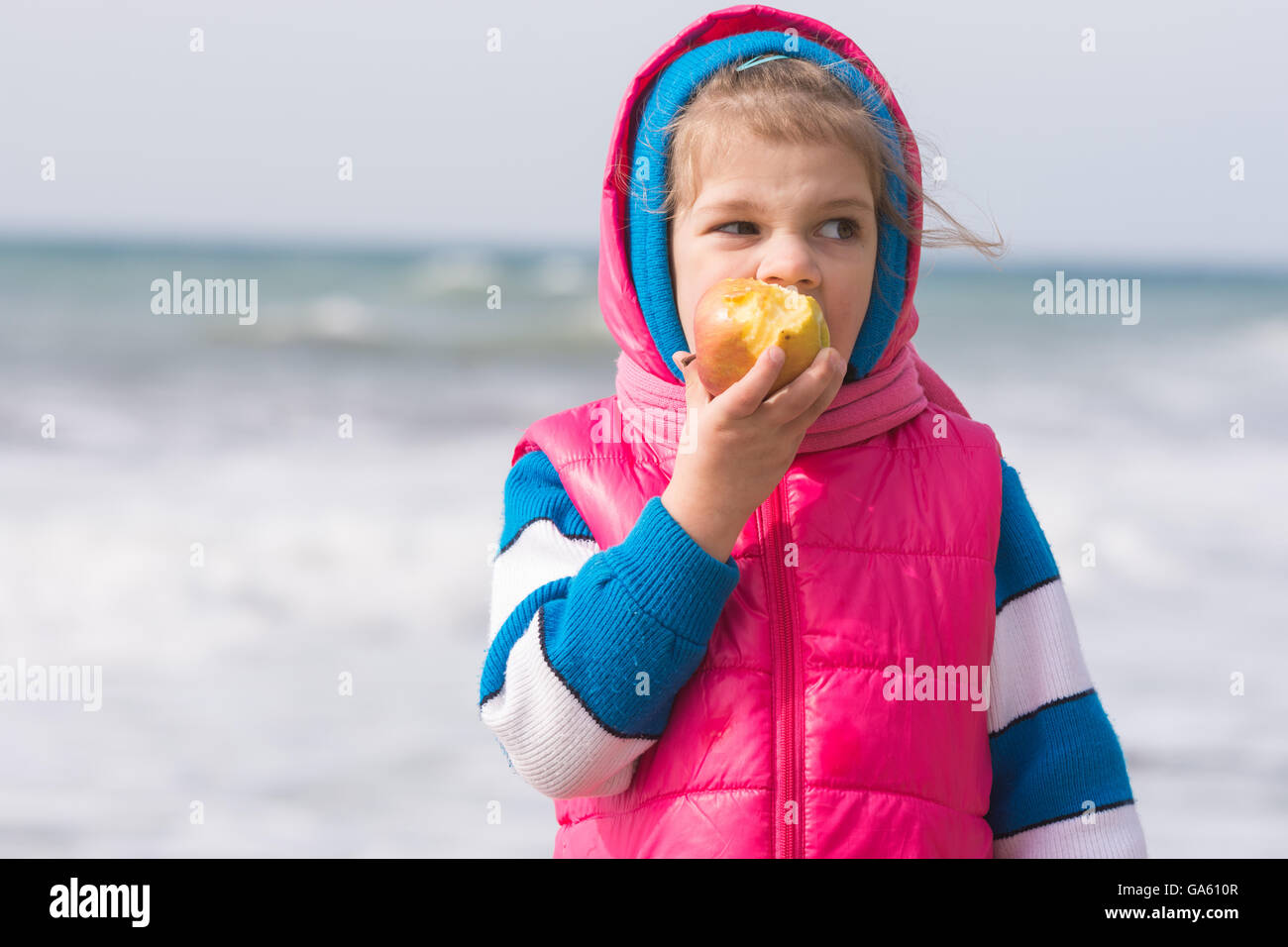 Five-year girl eating an apple on the background of the sea coast Stock Photo