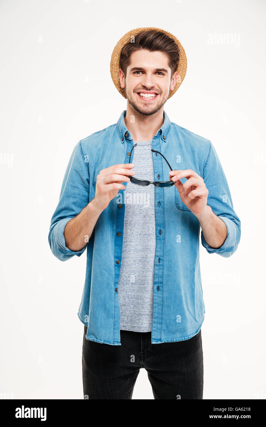 Cheerful confident young man in hat and blue shirt holding sunglasses ...