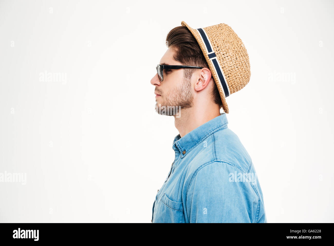 Profile of serious young man in blue shirt, hat and sunglasses over white background Stock Photo