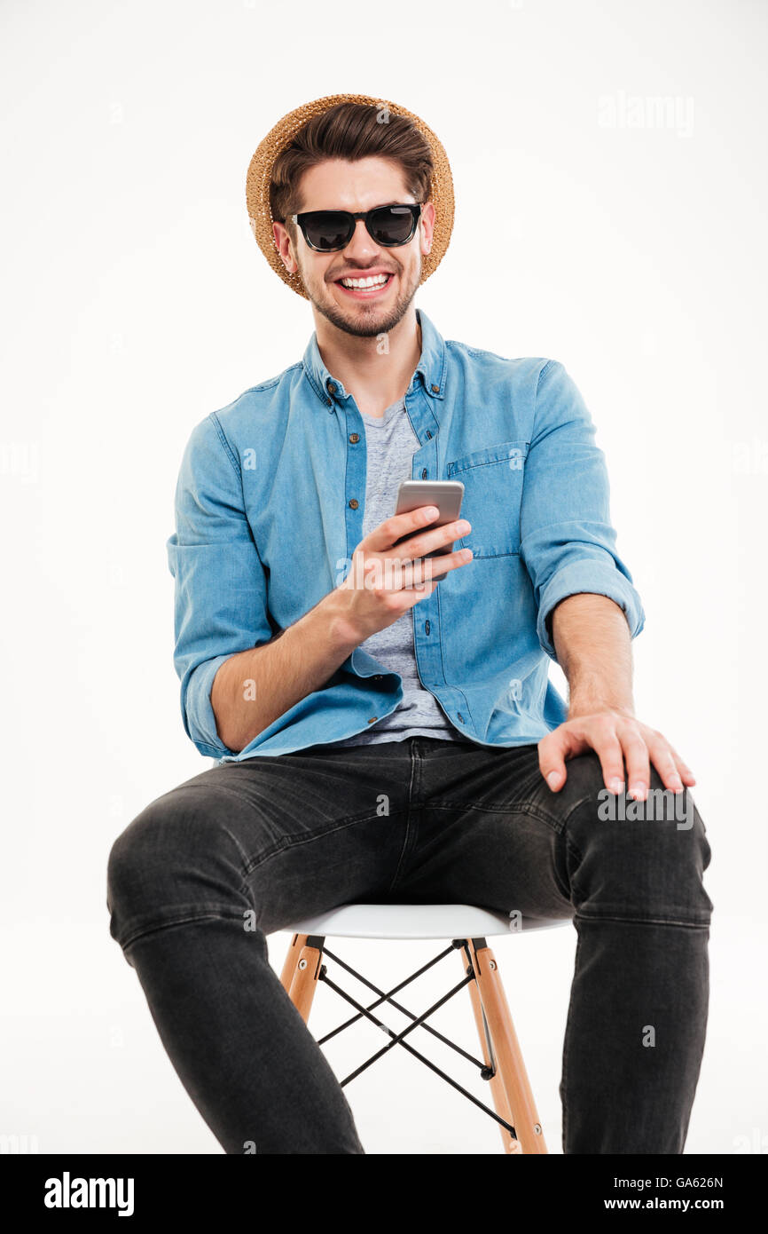 Happy young man in blue shirt, hat and sunglasses using mobile phone ...