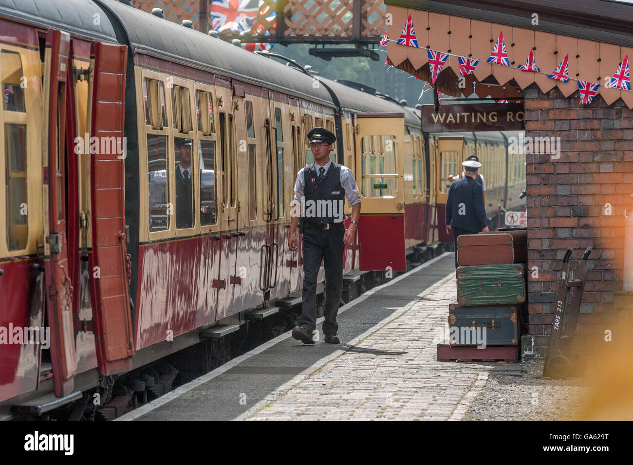 A train guard walking along the platform next to a steam train Stock Photo