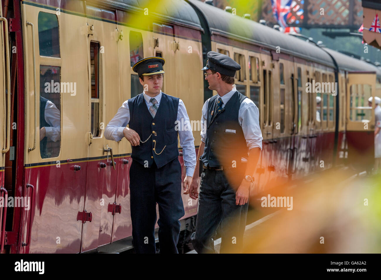 two train guards walking along the platform next to a steam train Stock Photo