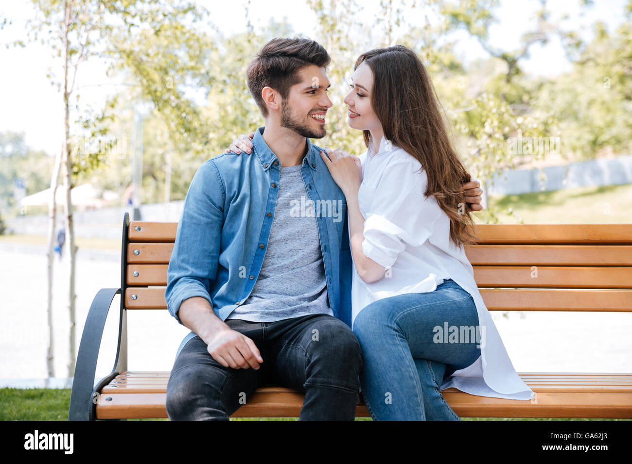 Happy young couple in love sitting on a park bench and looking at each ...