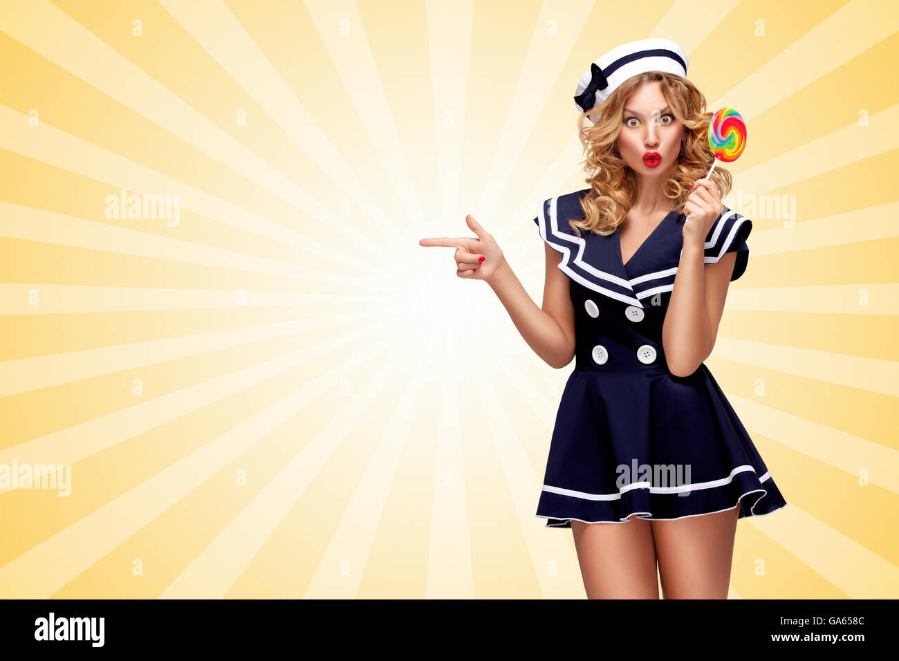 Surprised pin-up sailor girl with a lollipop pointing aside on cartoon style background. Stock Photo