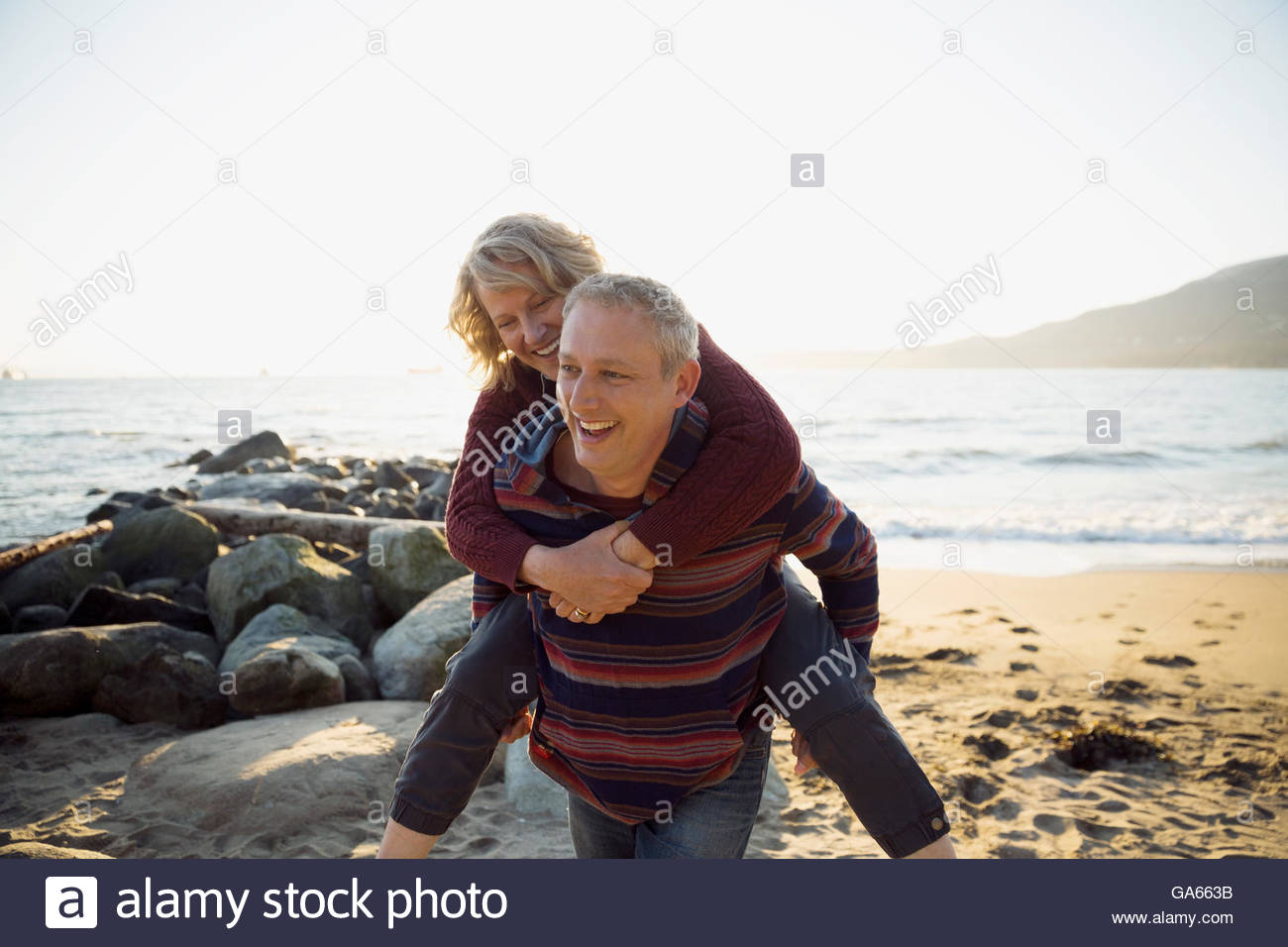 Portrait playful couple piggybacking on sunny beach Stock Photo - Alamy