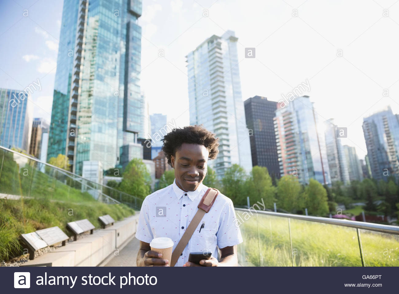 Businessman with coffee using cell phone in city below highrise buildings Stock Photo