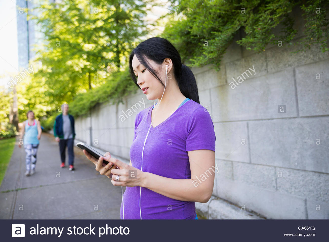 Pregnant woman with headphones using cell phone on city sidewalk Stock Photo