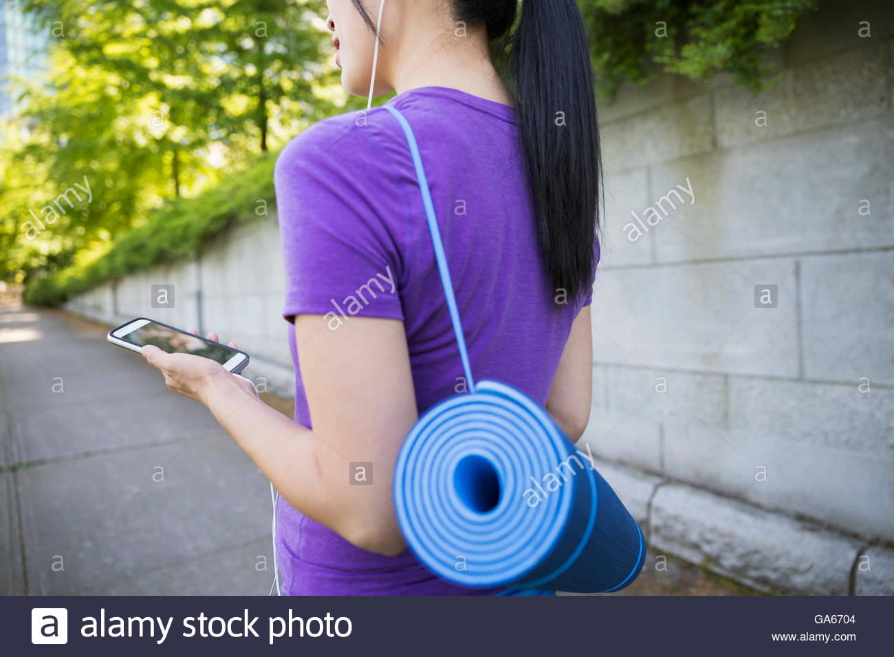 Pregnant woman with yoga mat and headphones using cell phone Stock Photo