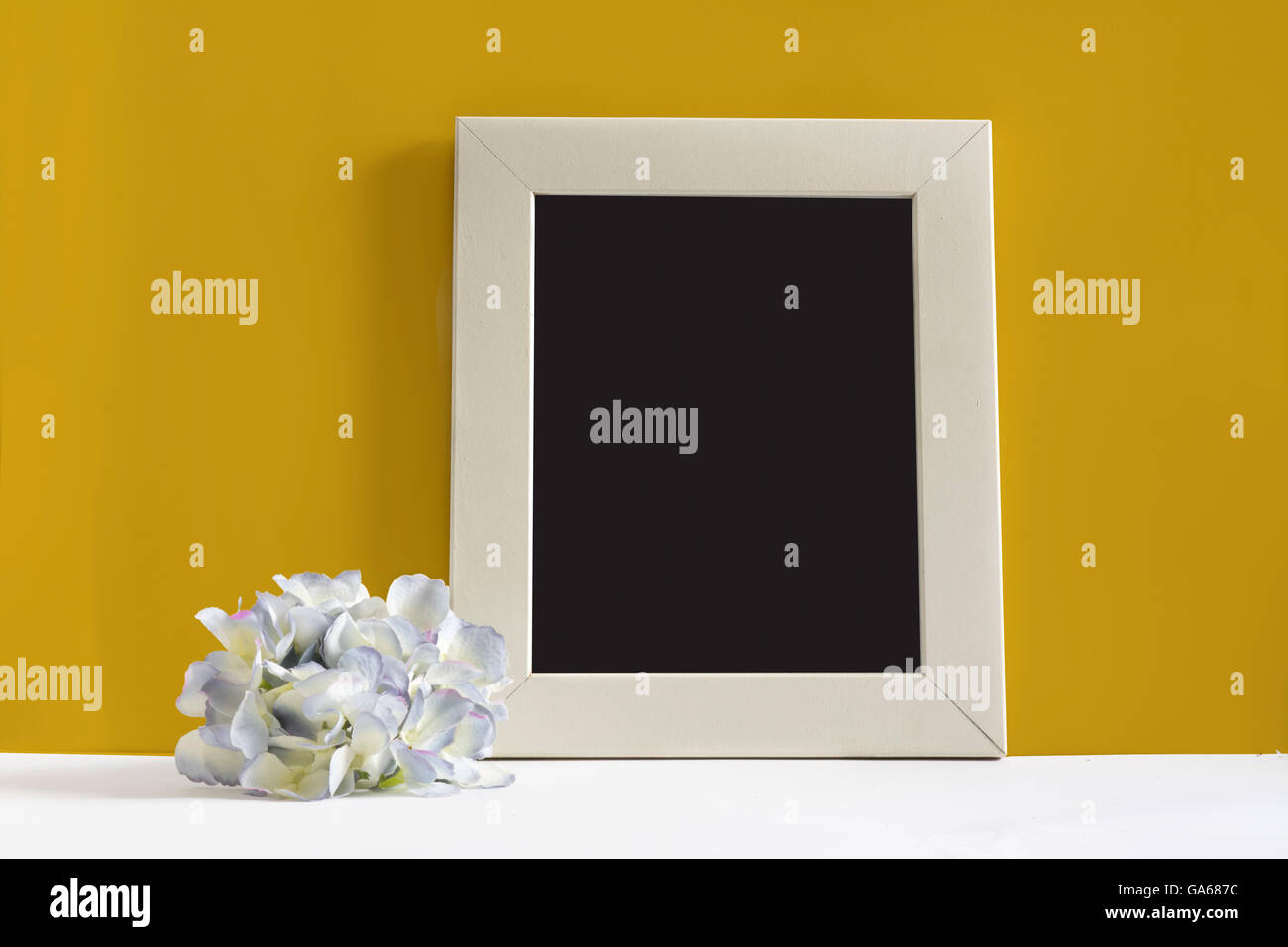 empty picture frame on yellow background, decorated with blue flower Stock Photo